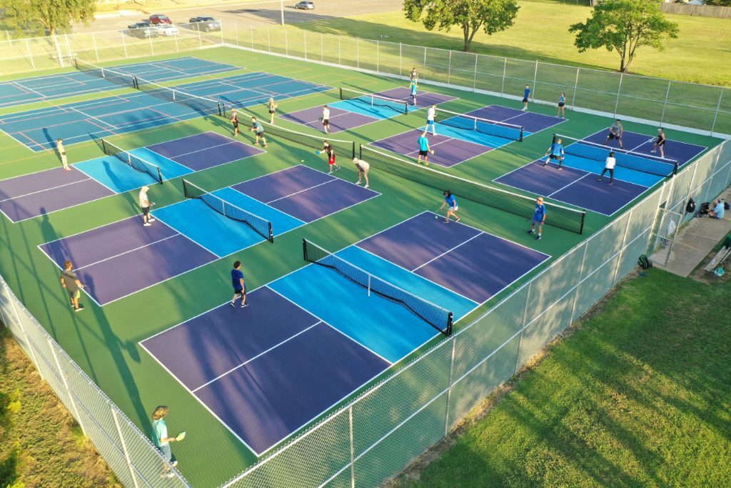 Aerial view of busy pickleball court complex with players on multiple blue and green SportMaster acrylic courts