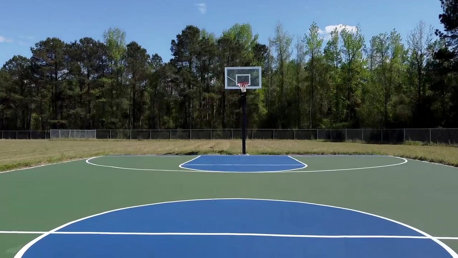 Finished blue and green outdoor basketball court with white lines and new goal, pines behind — East Arcadia, NC