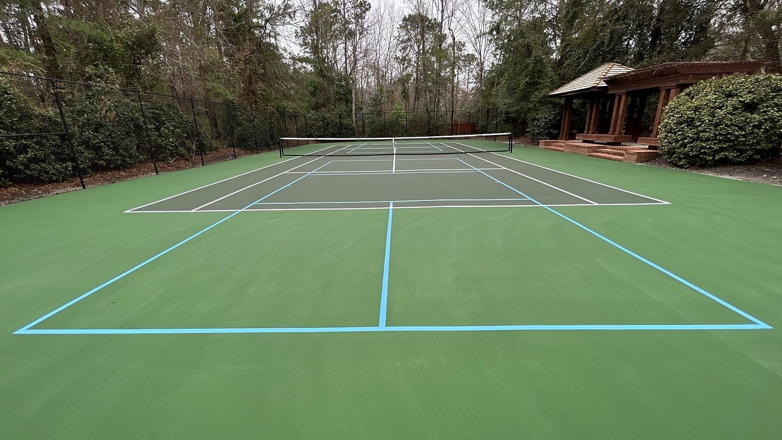 Resurfaced private tennis court with white tennis and light-blue pickleball lines, gazebo and pines behind — Wilmington, NC