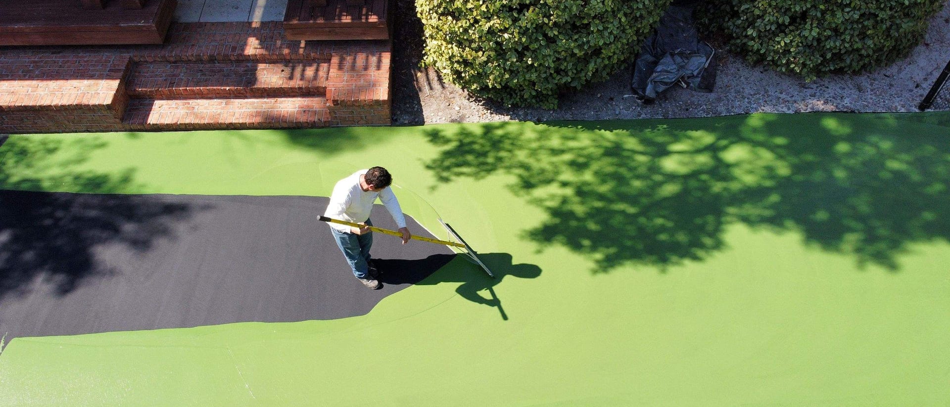 Drone view of a Waatti crew member squeegeeing bright green acrylic coating onto a backyard sport court — Wilmington, NC