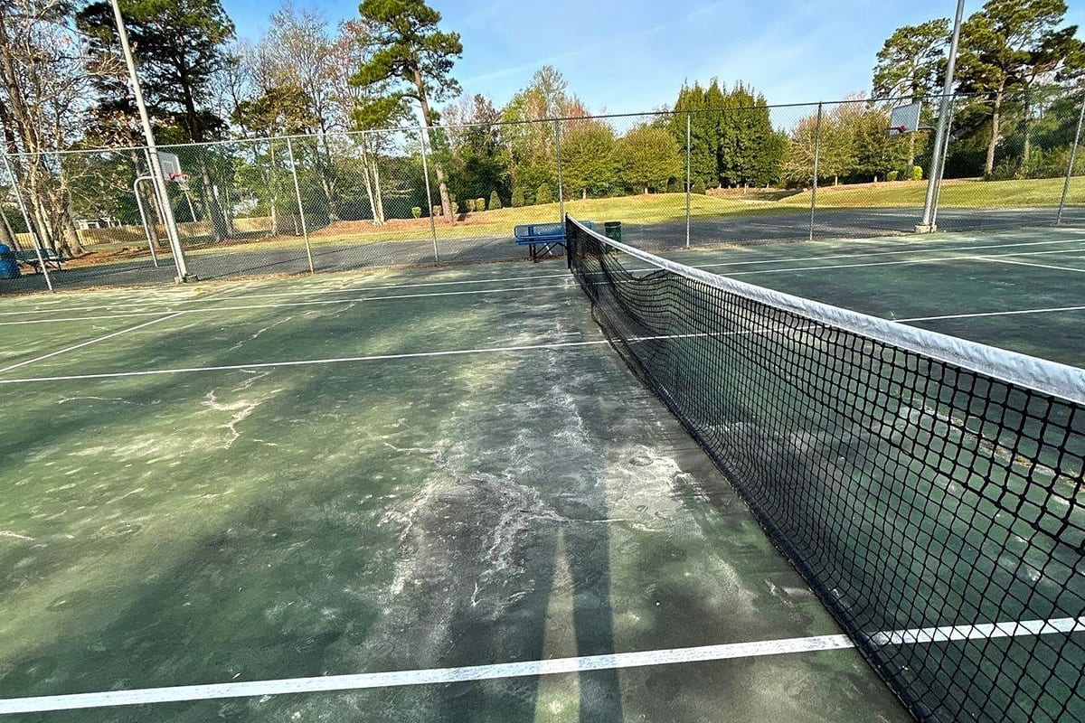 Before resurfacing: faded, stained tennis court surface along the net — Castle Hayne, NC